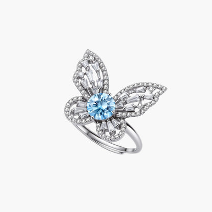 Sterling silver ring with blue moissanite center stone surrounded by clear stones in butterfly wing pattern on white background